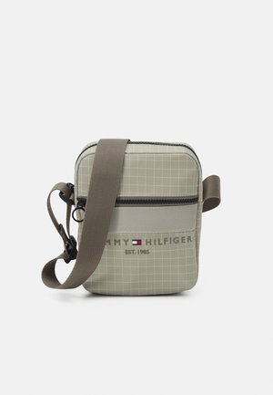 Petit sac bandoulière beige avec motif quadrillé, sangle marron réglable, poche avant zippée et logo Tommy Hilfiger avec drapeau et texte.