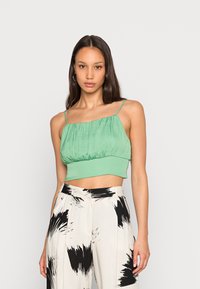 Top verde corto com um tecido texturizado, apresentando um corpete franzido e alças finas, combinado com calças largas de padrão preto e branco.