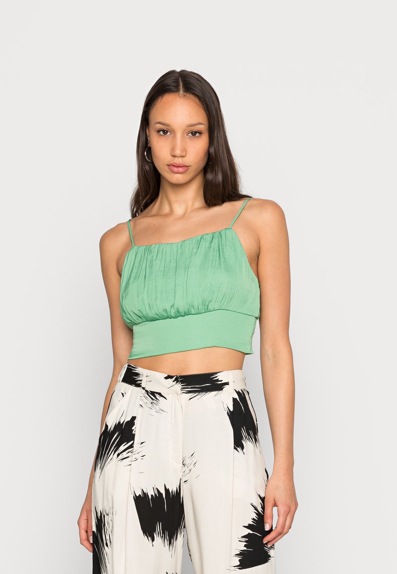 Top verde corto com um tecido texturizado, apresentando um corpete franzido e alças finas, combinado com calças largas de padrão preto e branco.