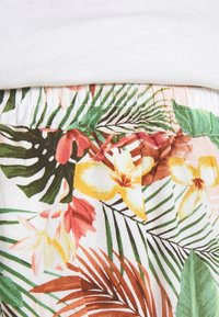 Tessuto a stampa floreale tropicale con foglie di palma verdi, fiori gialli e rosa, e una cintura elastica su un indumento bianco.