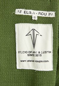 Tissu texturé vert avec une étiquette blanche comportant du texte imprimé noir et un logo, indiquant "STUDIO D'ART & DE DESIGN DEPUIS 2018."