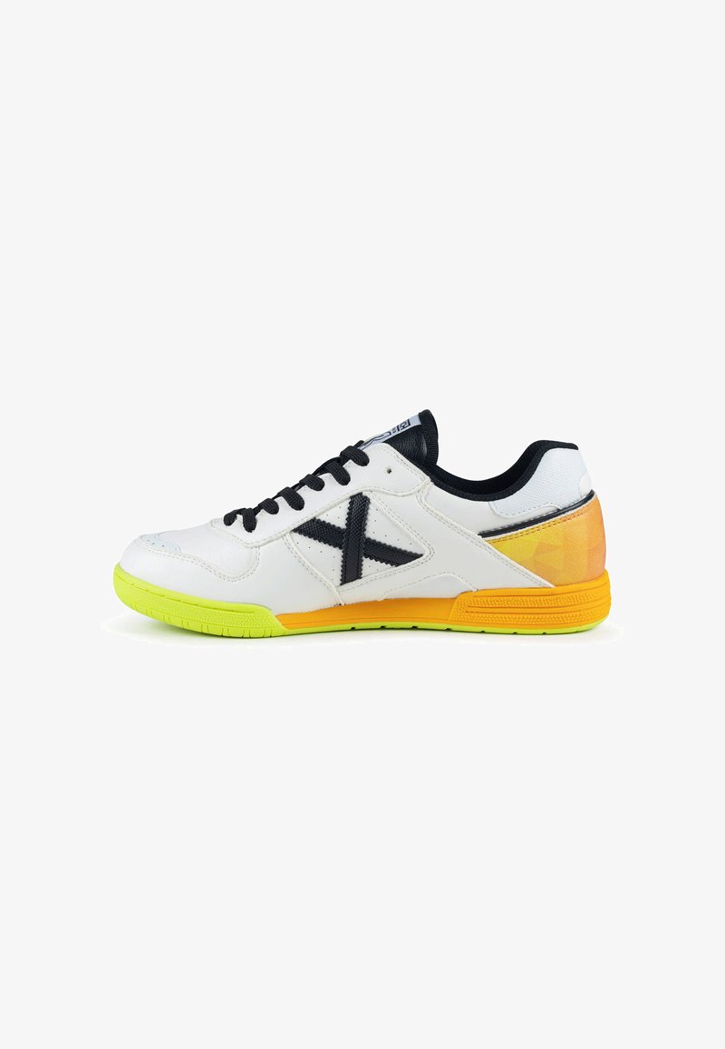 Chaussure de sport blanche avec lacets noirs, logo latéral noir, semelle avant vert néon et accents orange au talon et à la semelle intermédiaire.