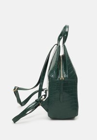 Zaino in ecopelle verde con texture a coccodrillo, design angolato, spallacci regolabili e dettagli in metallo dorato. Presenta una tasca laterale.