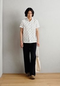White short-sleeve shirt with a subtle pattern, dark pants, and light-colored tote bag. Smooth texture, relaxed fit, and neutral colors.