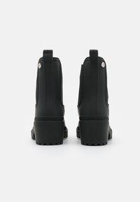 Botas negras de tobillo con parte superior de goma, acabado texturizado y tacón cuadrado. Presenta paneles laterales elásticos y un acento plateado cerca del tacón.