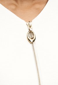 Κοντινή λήψη ενός χρυσού φερμουάρ σε λευκό ένδυμα, που δείχνει λεπτομερείς δοντάκια φερμουάρ και μερικό ντεκολτέ του φορέσαντος.