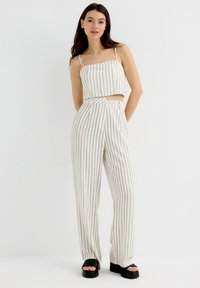Conjunto de top corto de rayas blancas y pantalones de pierna ancha, con tirantes finos, cierre de botones y una textura suave; combinado con sandalias de plataforma.