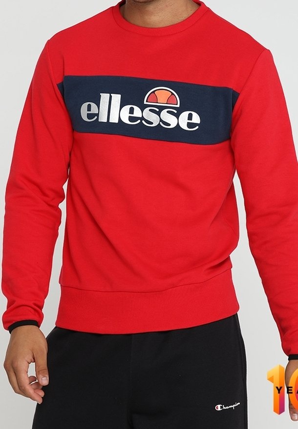 Sweat-shirt rouge avec une bande bleu marine sur la poitrine avec le logo blanc "ellesse" et un pantalon noir avec un petit logo Champion.