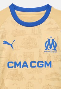 Žltý športový dres s modrými akcentmi, zdobený textúrovaným vzorom pamiatok. Výrazne zobrazené logo Puma a nápis "CMA CGM".