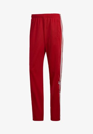 Pantalon de sport rouge en tissu léger, avec des bandes blanches sur les côtés, une ceinture élastique et des poches zippées.