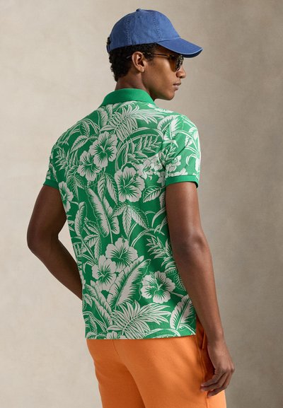 Πράσινο πόλο μπλουζάκι με λευκό λουλουδάτο μοτίβο, κοντά μανίκια και αντίθετο γιακά· συνδυασμένο με πορτοκαλί παντελόνι. Μπλε καπέλο ολοκληρώνει την εμφάνιση.