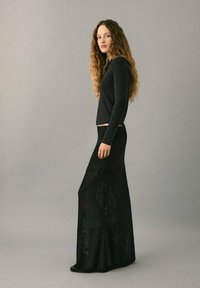 Top negro de manga larga y falda maxi negra texturizada. La falda presenta un diseño de malla con patrones sutiles y una cintura ajustada.