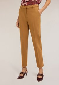Béžové kalhoty s úzkým střihem, s poutky na opasek a bočními kapsami. Nosené s burgundy lodičkami z lakové kůže, které mají detail pásku.