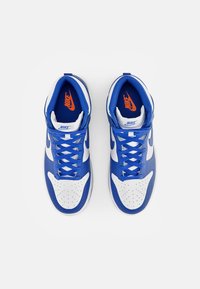 Zapatillas Nike en azul y blanco, hechas de materiales de malla y cuero, con perforaciones, cordones azules y un logo naranja en la plantilla.