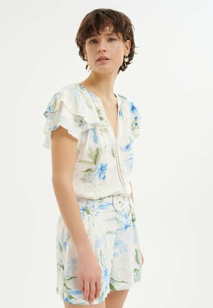 Bloemige outfit met een witte basis en blauwe en groene bloemen, gerimpelde mouwen en een tailleband met een ronde gesp. Korte broek inbegrepen.