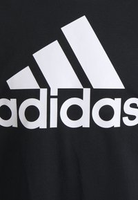 Czarny bawełniany t-shirt z dużym białym logo Adidas. Logo zawiera trzy ukośne paski oraz nazwę marki w pogrubionych, wielkich literach.
