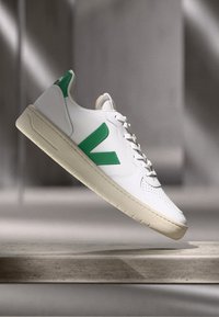 Biežas baltas ādas sporta apavu ar zaļiem akcentiem, noapaļota pirksta daļa, perforēta apdare, plakanas šņores un teksturēta pelēkbalta zole.