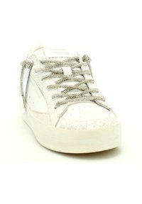 Zapatilla blanca con textura de cuero agrietado, cordones planos en tono plateado, puntera redondeada y suela texturizada. La marca en la lengüeta es visible.