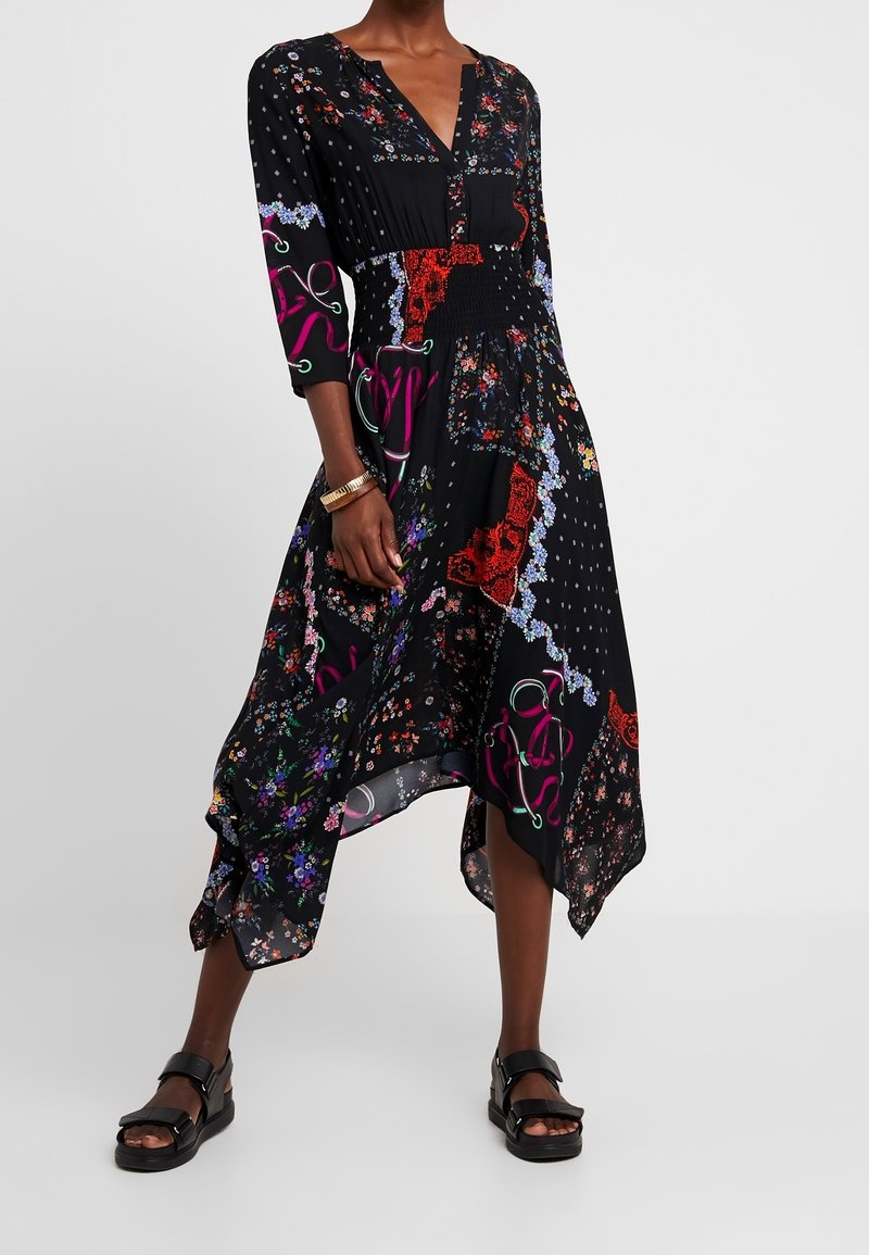 Robe noire avec des motifs floraux et abstraits, décolleté en V, manches trois-quarts, ourlet asymétrique, tissu léger et coupe ample.