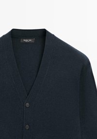 Tmavě modrý vlněný kardigan s V-výstřihem, se čtyřmi ladícími knoflíky vpředu a měkkým, texturovaným povrchem.