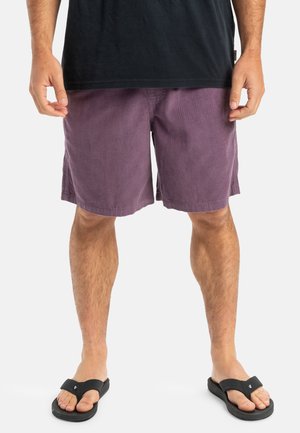 Purple corduroy shorts with a relaxed fit, featuring side pockets and worn with black flip-flops. The fabric has a ribbed texture.