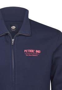 Mornarska zip up trenerka z rebrastim ovratnikom in rožnato vezenim logotipom. Mehka tkanina, z zadrgo na sprednji strani in udobno prileganje.