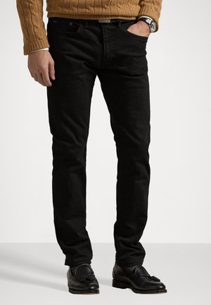 Schwarze Jeans mit gerade geschnittenem Schnitt, aus strukturiertem Denim, mit klassischem Fünf-Taschen-Design, getragen mit schwarzen Loafers.