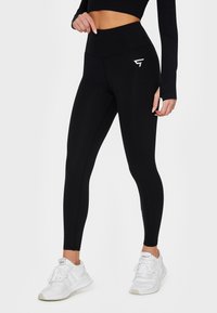 High-waisted black leggings with a smooth texture, featuring a white logo on the thigh and a fitted design for activewear.