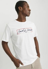 Hvid kortærmet t-shirt med et marineblåt og rødt logo "Jack & Jones" med "SINCE 1990" inde i en rektangulær ramme. Glat tekstur.