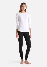 Haut à manches longues blanc avec un col rond, associé à des leggings noirs ajustés. La tenue présente une texture lisse et un design simple.