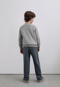 Light gray knitted sweater with ribbed cuffs and hem, paired with dark gray textured pants. The person is viewed from the back.