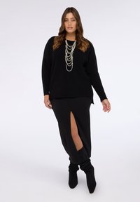 Schwarzer gestrickter Pullover mit lockerem Schnitt, kombiniert mit einem schwarzen Maxirock mit hochgeschlossenem Schlitz am Oberschenkel. Akzente gesetzt durch mehrschichtige Perlenketten.