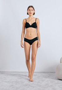 Set de lenjerie neagră, ce include un sutien fără cusături, ușor buretat, cu bretele ajustabile și chiloți tip bikini asortați cu margine din dantelă. Textură netedă.