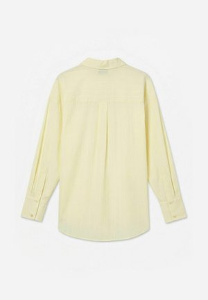 Hosszú ujjú, halványsárga ing gombos mandzsettákkal, hátsó nyereggel és középső redővel, hátulról fehér háttéren bemutatva.