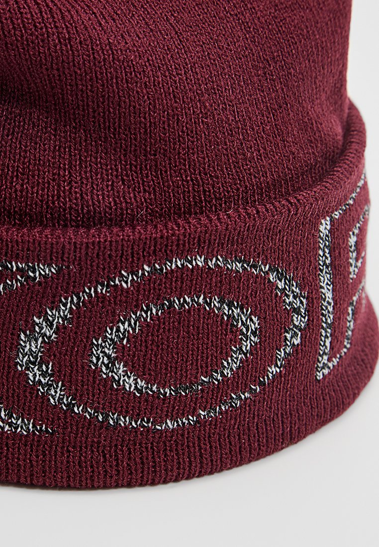 Bordeauxfarbene Strickmütze mit geripptem Muster und weißer gestickter Schrift rund um den Bund. Weicher, dehnbarer Stoff für hohen Tragekomfort.