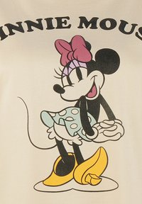 Personaje de dibujos animados en blanco y negro con un lazo rosa, vistiendo una falda azul con lunares y zapatos amarillos, sobre un fondo de tela de color claro.