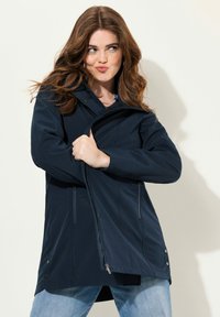 Tummansininen vedenpitävä takki hupulla, vetoketjulla ja sivutaskuilla, joka on valmistettu sileästä kankaasta ja istuu hyvin.