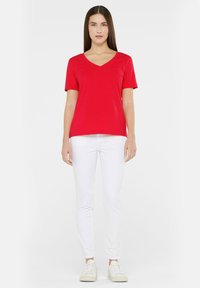 Red, short-sleeve V-neck t-shirt made of smooth fabric, paired with white fitted pants and white sneakers. Simple design with no patterns.
