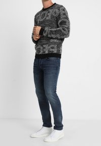 Pull en tricot à motif noir et blanc avec un col rond, associé à un jean bleu foncé et des baskets blanches. Tissu texturé et poignets côtelés.