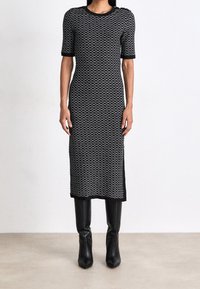 Dopasowana dzianinowa sukienka w czarno-białe fale, z krótkimi rękawami, okrągłym dekoltem i slim fit, zestawiona z dopasowanymi czarnymi skórzanymi botkami.