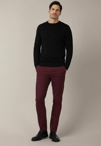 Czarny sweter z dzianiny, bordo spodnie i czarne buty. Sweter ma okrągły dekolt; spodnie są slim-fit. Całość ma gładką fakturę.