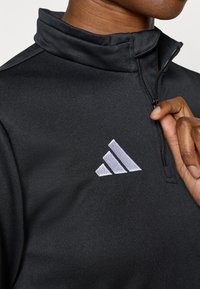 Μαύρο μπουφάν με φερμουάρ και ψηλό γιακά, κατασκευασμένο από υφασμένο ύφασμα. Διακοσμείται με γκρίζο κεντημένο λογότυπο στην αριστερή πλευρά.