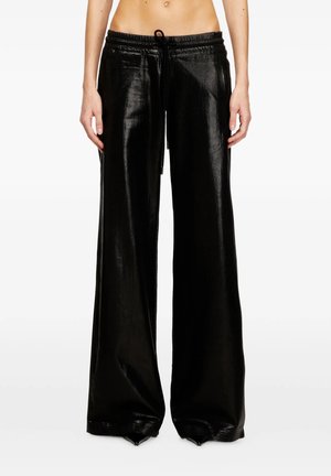 Pantaloni neri a gamba larga con texture lucida e coulisse in vita, indossati da una persona con il ventre scoperto, in piedi davanti a uno sfondo bianco.