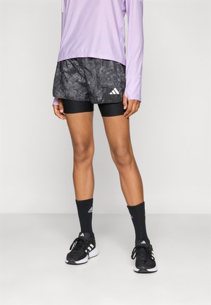 Svarte og grå mønstrede shorts kombinert med en lys lilla langermet skjorte, svarte sokker og svarte treningingssko.