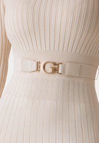 Ceinture élastique beige avec une boucle en forme de G ton or, en matériau lisse au design élégant. Idéale pour cintrer la taille.