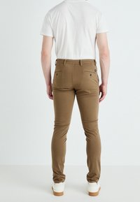 Hnědé slimm-fit kalhoty s zadními kapsami, elastickým pasem a hladkým povrchem, spárované s jednoduchým bílým tričkem a bílými teniskami.