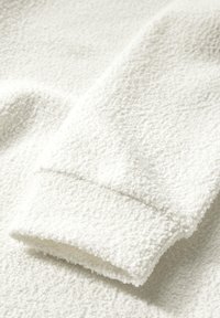 Tejido de forro polar blanco con una textura suave, que presenta un puño enrollado y una superficie ligeramente texturizada. El material parece cálido y acogedor.