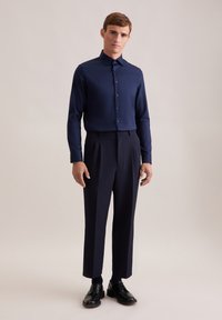 Marineblauw overhemddas met lange mouwen, gecombineerd met hoog-gefitte, op maat gemaakte donkere broeken en zwarte leren schoenen. Gladde stof, aansluitend ontwerp.