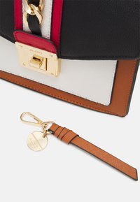 Černá, bílá, červená a hnědá kožená kabelka s pozlacenými hardwarovými detaily, vedle hnědého koženého klíčenky se zlatou sponou a štítkem.