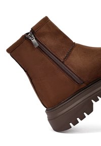 Bruine suède enkellaars met een zijrits, rubberen zool en een gekarteld profiel. Beschikt over een gladde textuur en minimale stikdetails.